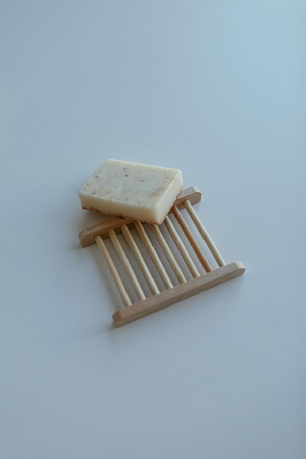 A minimalist photo of a bar of soap resting on a wooden soap dish against a white background.