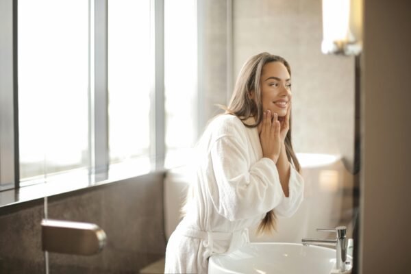 A woman in a bathrobe smiling at her reflection in a modern bathroom.