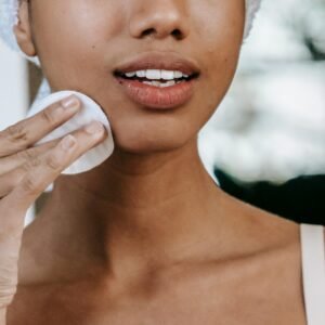 Crop anonymous ethnic female with pure skin touching cheek with cotton disk during daily routine at home