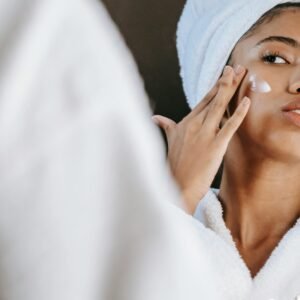 Woman in a bathrobe practices her skincare routine with moisturizing cream. Perfect for wellness themes.