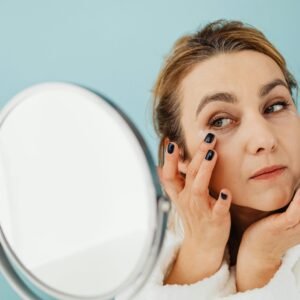 A woman in a bathrobe applies skincare cream while looking in the mirror. Ideal for beauty and self-care concepts.