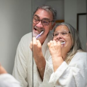 Happy senior couple brushing teeth together in the bathroom mirror emphasizing dental hygiene.