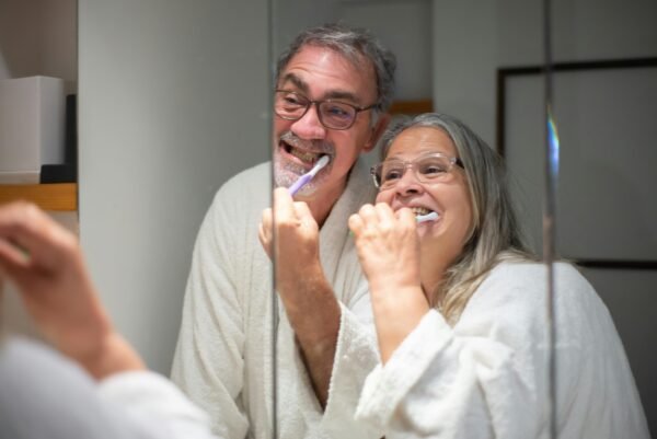 Happy senior couple brushing teeth together in the bathroom mirror emphasizing dental hygiene.