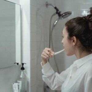 Woman brushing teeth in a modern bathroom, promoting daily oral health habits.