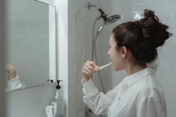 Woman brushing teeth in a modern bathroom, promoting daily oral health habits.