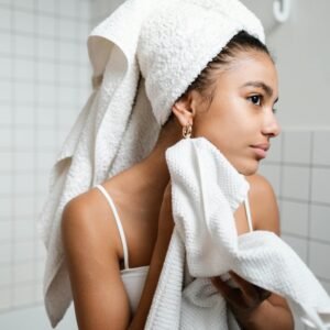 Young woman drying face with towel during morning skincare routine in a modern bathroom.