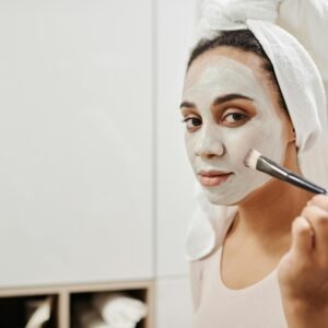 Adult woman using a makeup brush to apply a facial clay mask as part of her skincare routine at home.