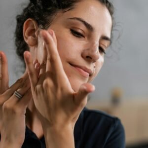 Close-up of a woman applying skincare product to her face, emphasizing healthy skin and care routine.