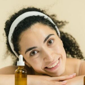 Woman with curly hair smiling, showcasing skincare products, indoors.
