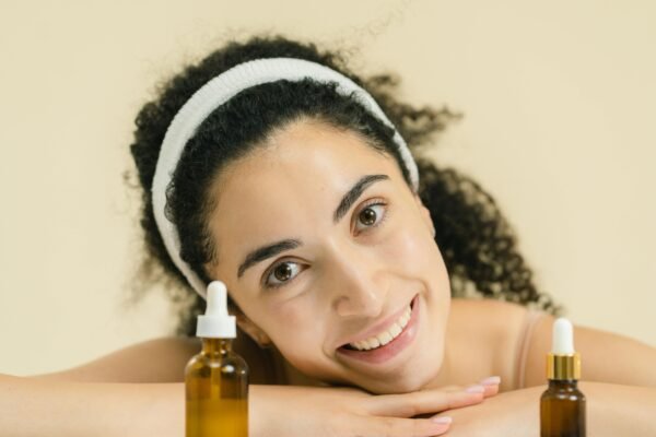 Woman with curly hair smiling, showcasing skincare products, indoors.