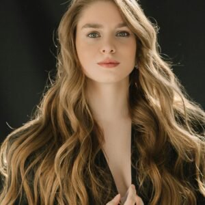 Close-up portrait of a young woman with long, wavy blonde hair against a black background.