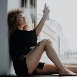 Young woman relaxing by a window while applying hydrating spray, enjoying a tranquil moment.