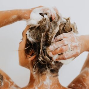 Back view of a woman washing her hair in a shower with white background.