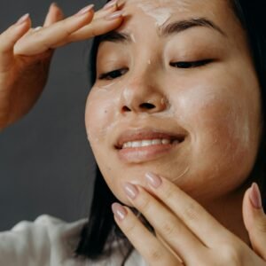 Smiling Asian woman applying face cream as part of her skin care routine on a gray background.