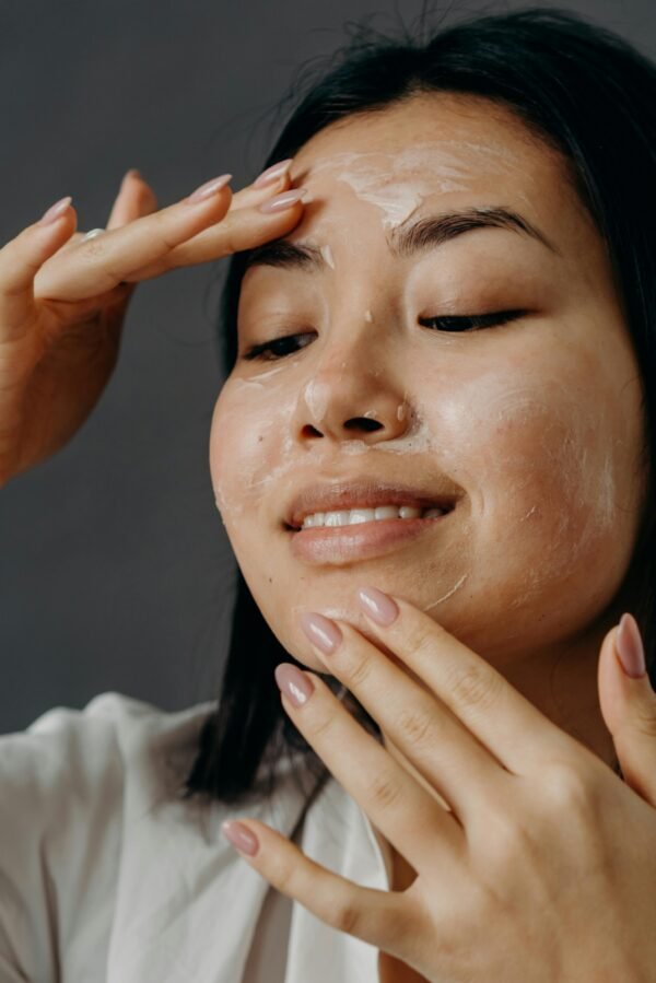 Smiling Asian woman applying face cream as part of her skin care routine on a gray background.